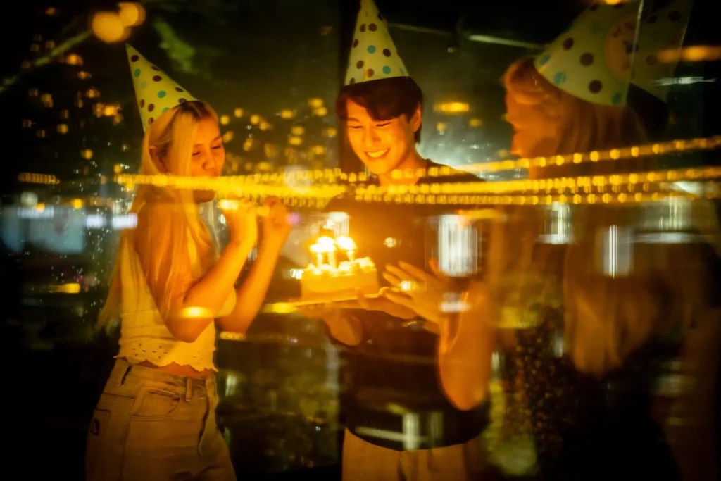 Friends in party hats bringing out a birthday cake with candles