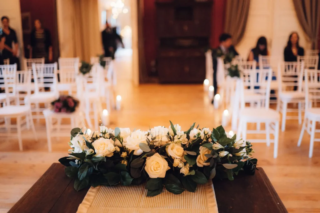 A candlelit ceremony aisle with white chairs and a floral garland